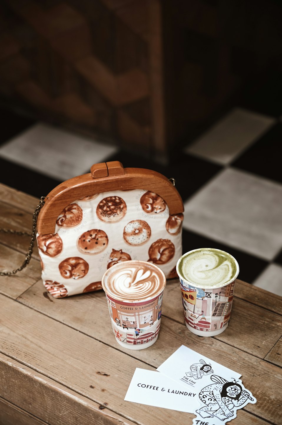 Latte and matcha drinks beside a novelty purse on a wooden table.